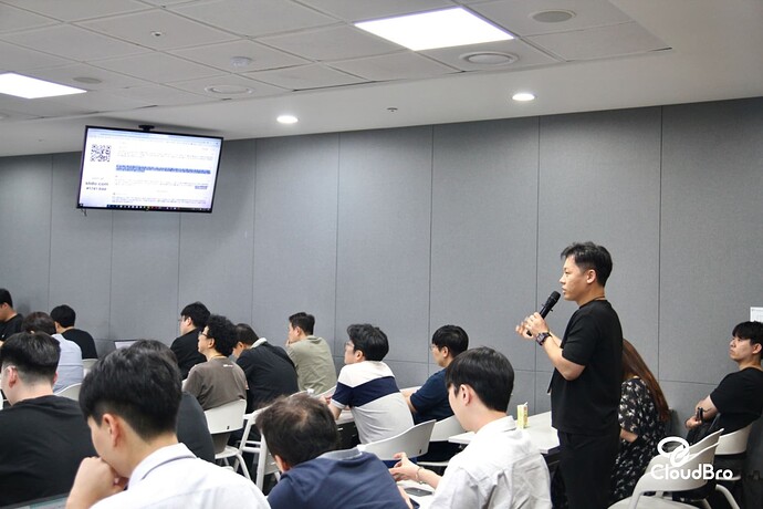 A room with people listening attentively to a speaker presenting a slide on a screen, while a presentation or meeting is being conducted. (Captioned by AI)