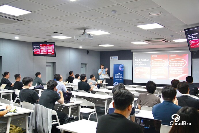 The image depicts a seminar or lecture taking place in a well-lit conference room, with attendees facing the front where a presenter is giving a speech. (Captioned by AI)