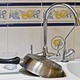 A kitchen sink with a pan, a glass, and a spoon sitting on the counter next to it.